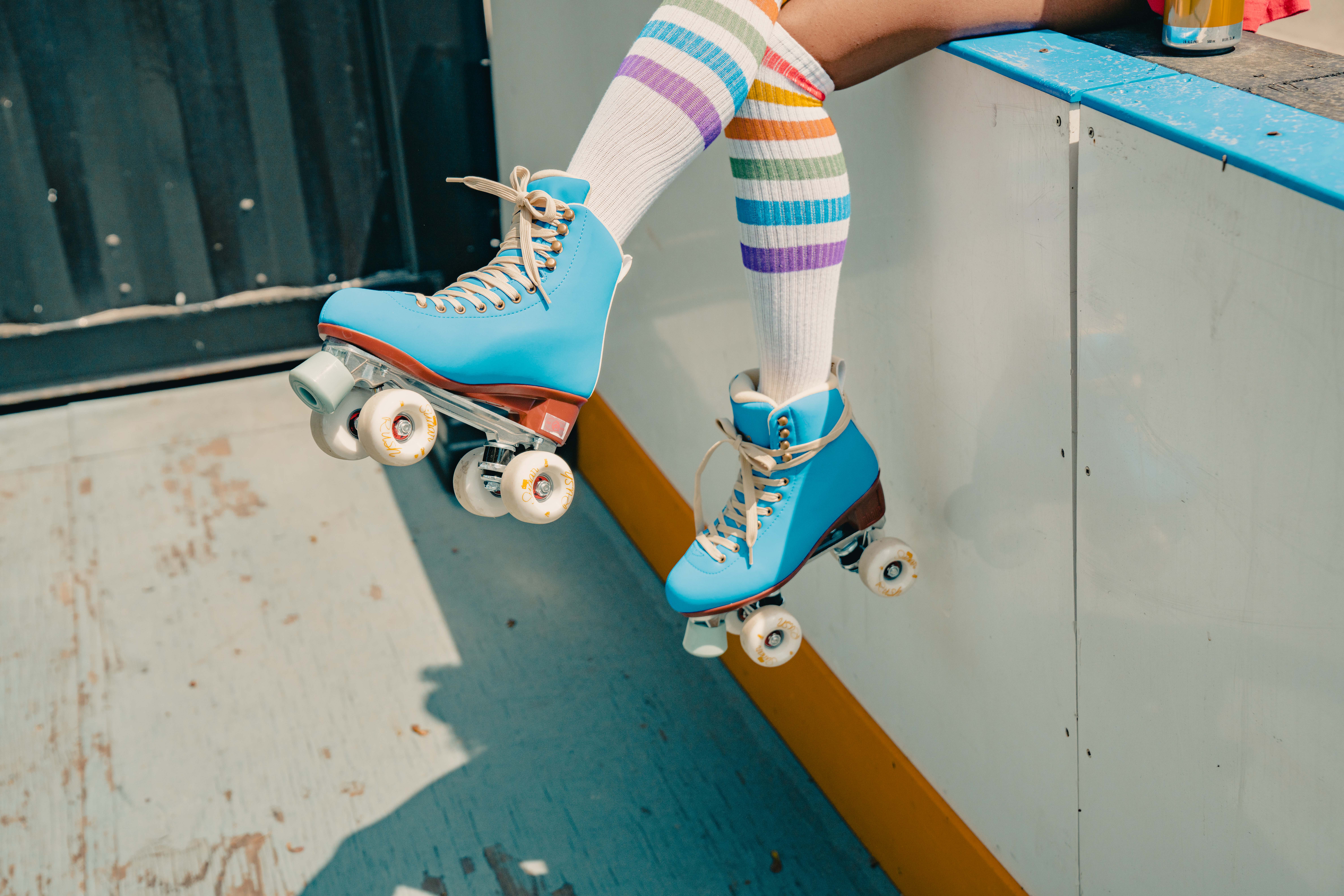 The lower half of someone's leg hang over a bench. They're wearing blue rollers skates on their feet.
