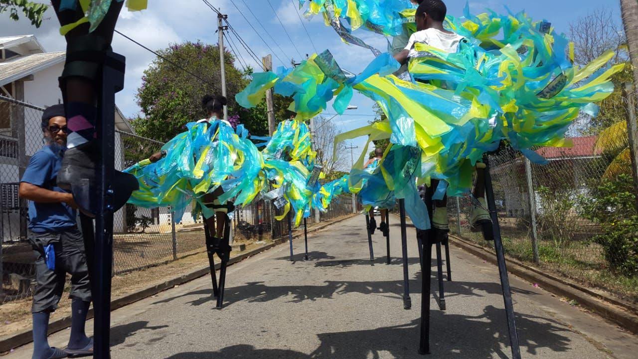 A group of people wearing elaborate bright costumed walk on stilts in a procession.