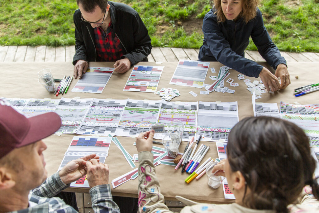 Four people sit around a picnic table with papers and markers in front of them.